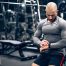 Muscular man in gym checking his watch between sets, symbolizing time-efficient strength training for busy people.
