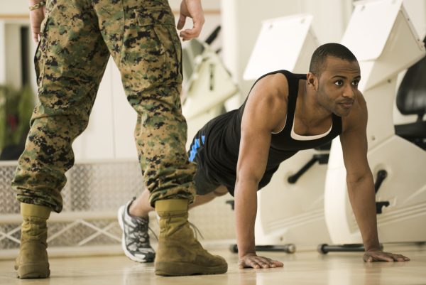 Bootcamp fitness trainer standing over trainee for accountability as he does pushup