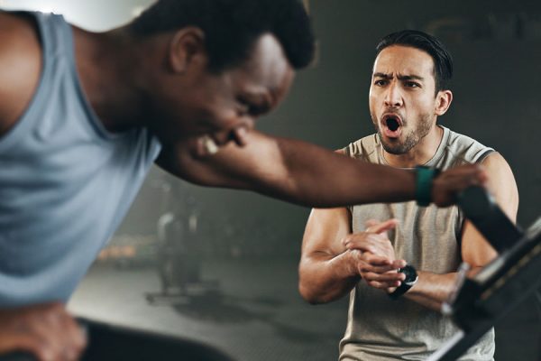 Man on exercise bicycle with personal trainer for motivation and accountability