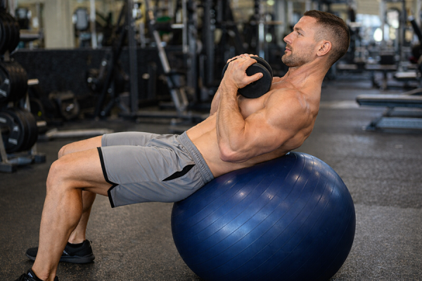 Man training abs with weight on stability ball